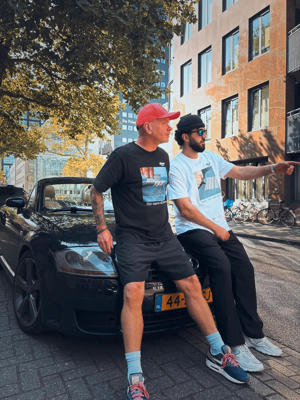 Two men lean against a black convertible.