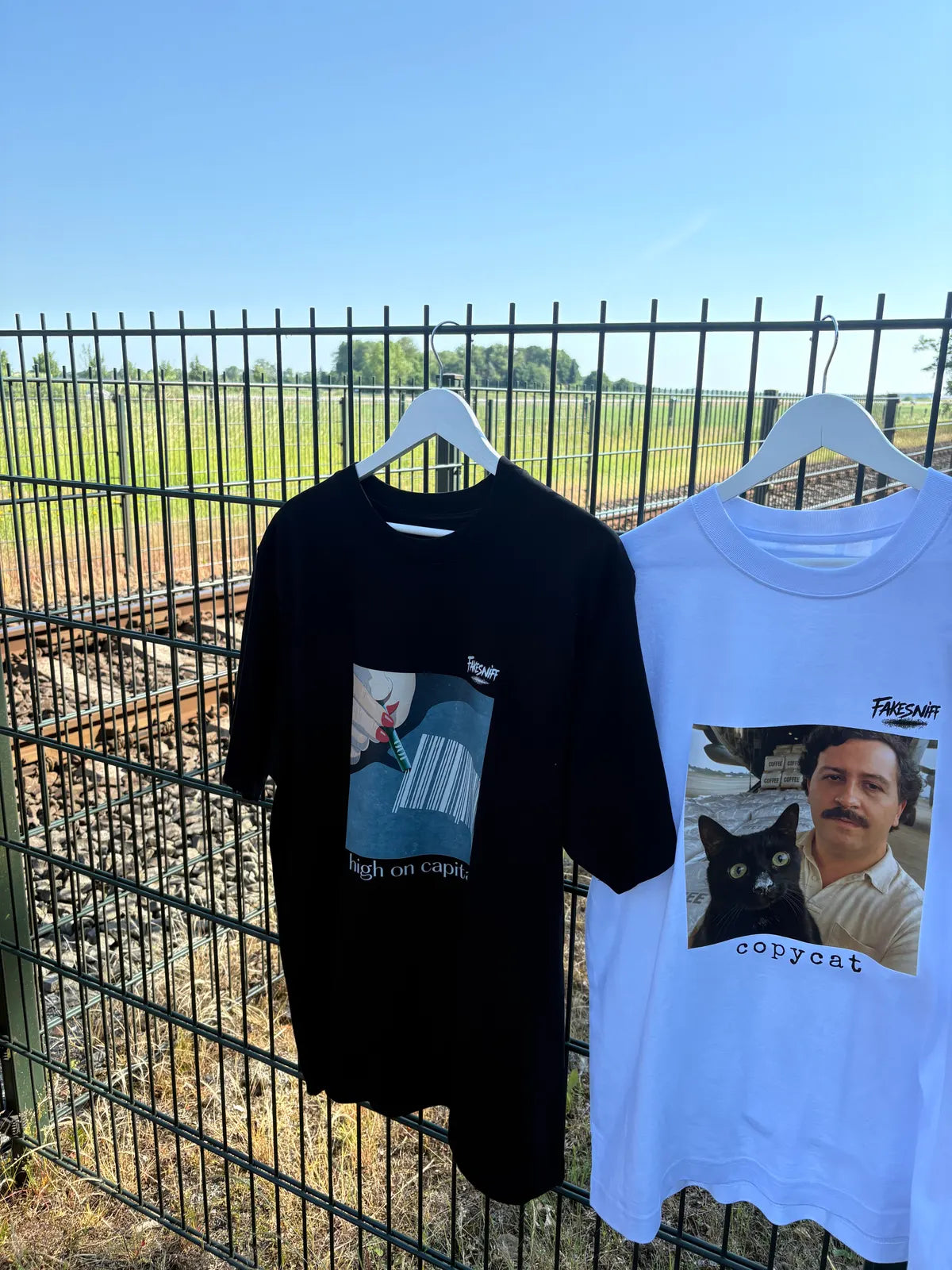 Two shirts on hangers on a fence, with the railway behind them.