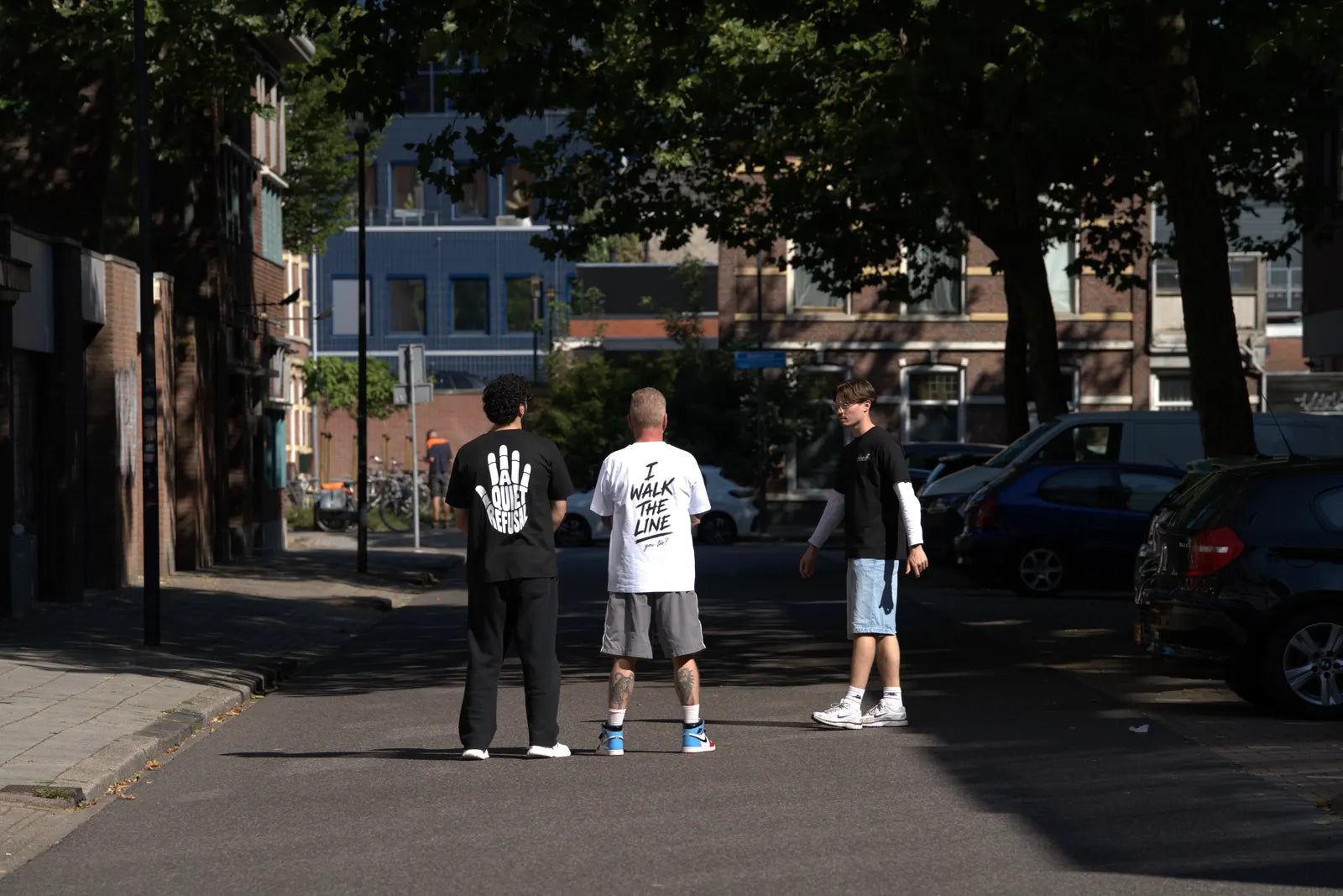 Three men stand in the street with their backs to the camera.