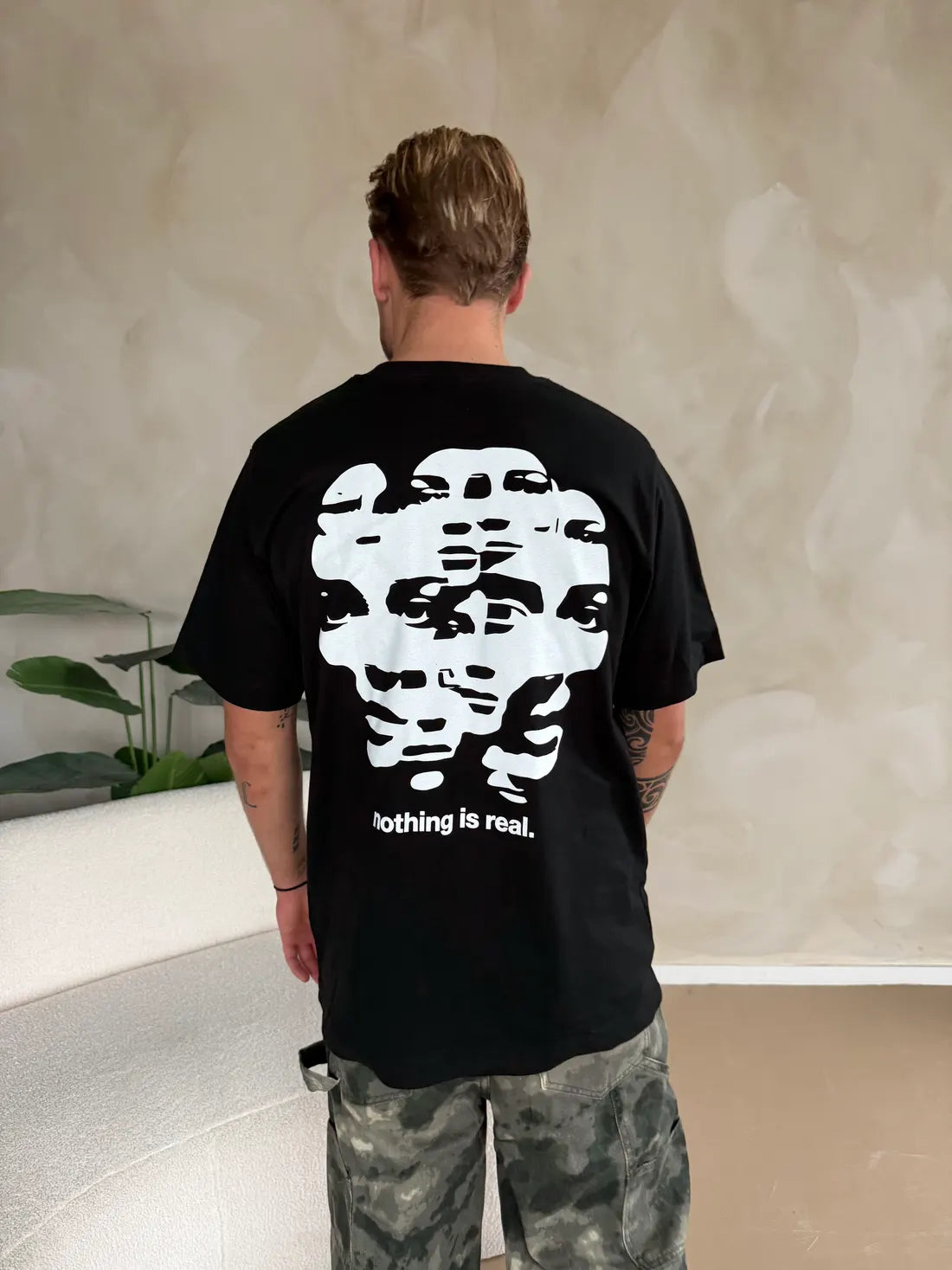 The back of a black shirt with a print of overlapping faces and the words nothing is real.