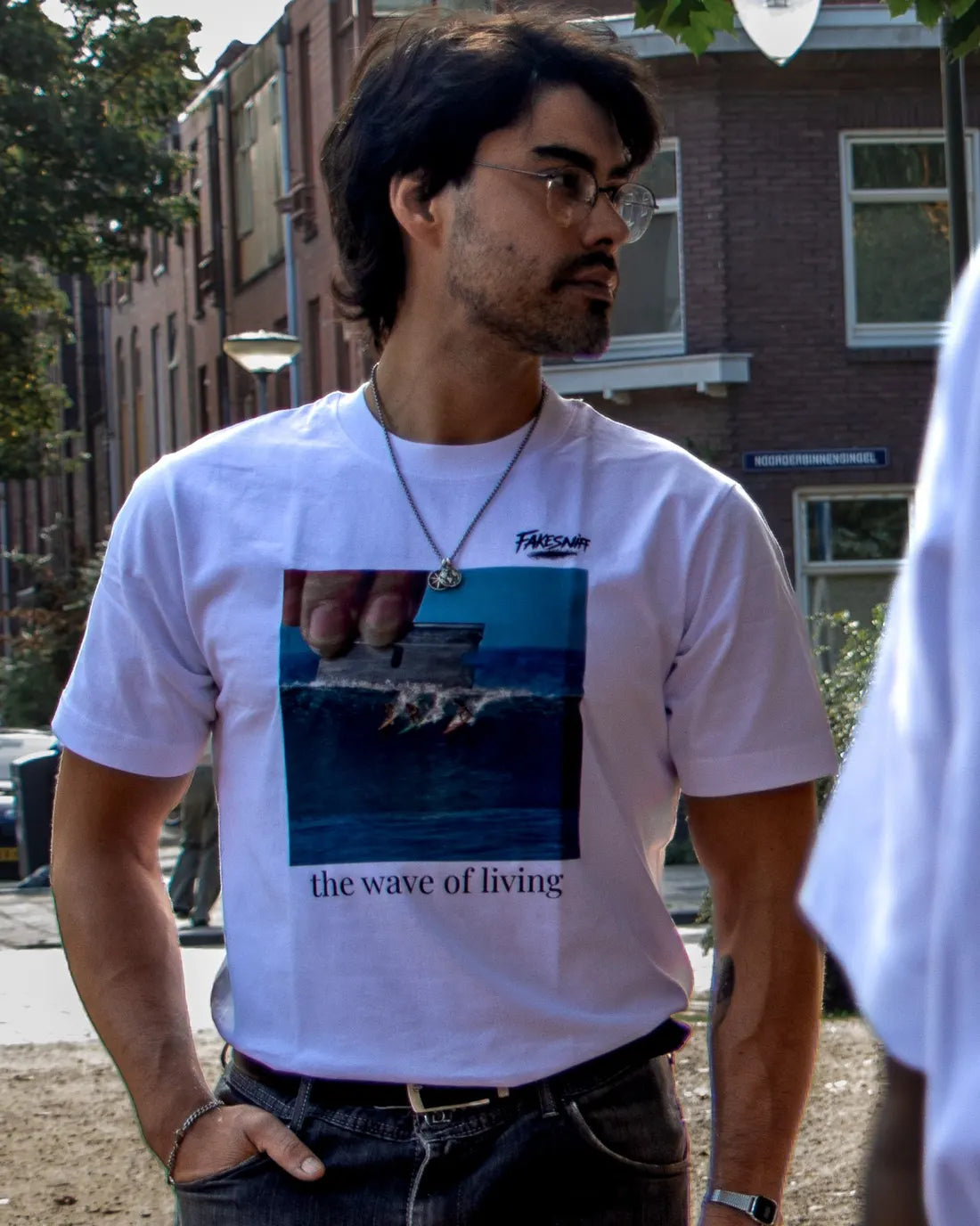 A man wearing glasses in the street, with houses behind him.